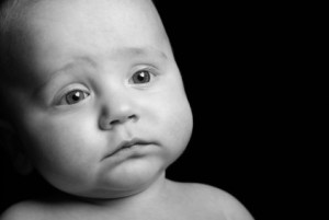 Baby with a sad expression on his face and heart shaped catch lights in his eyes representing love.  Isolated on Black.